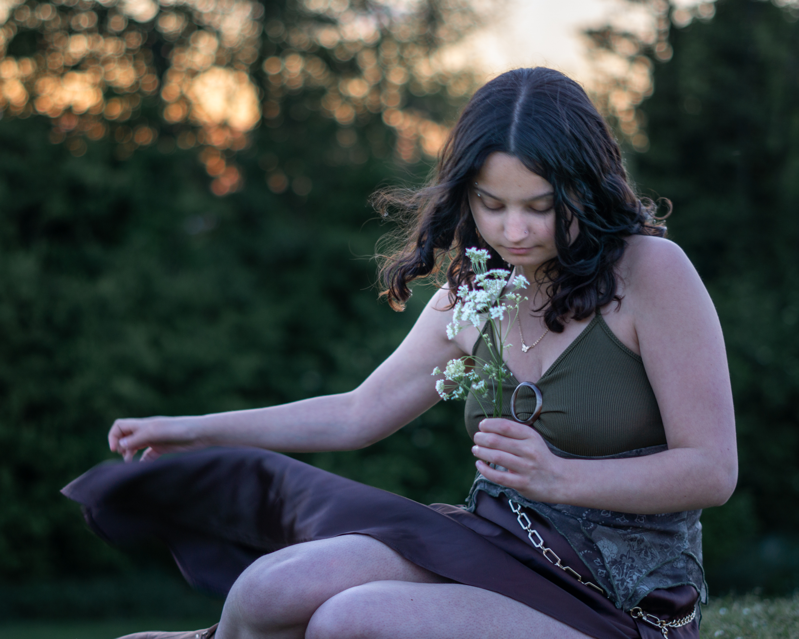 A woman dressed as a fae sitting with her legs to the side, her dress flapping in the wind.