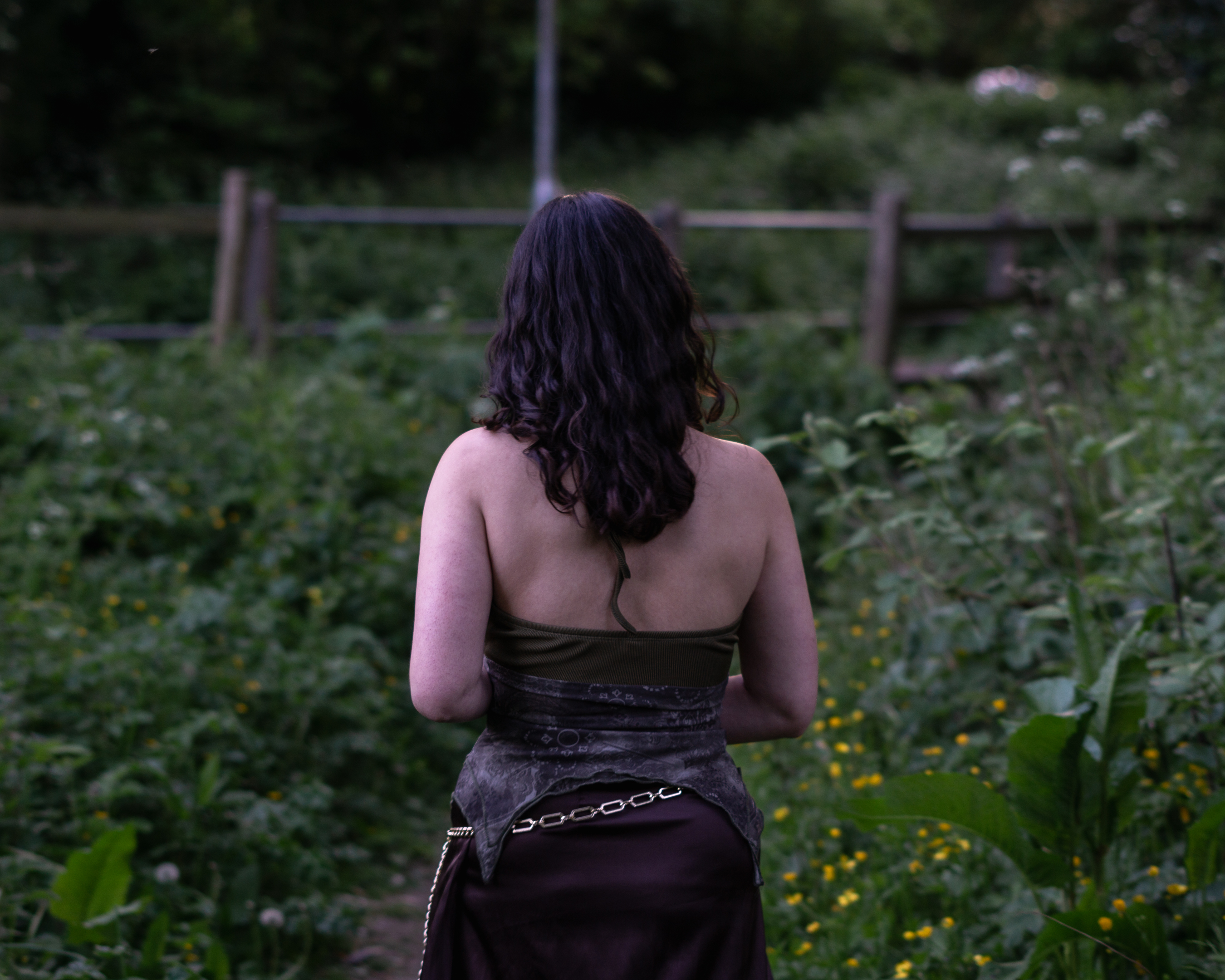 A woman dressed as a fae standing with her back turned in the middle of a nature path.