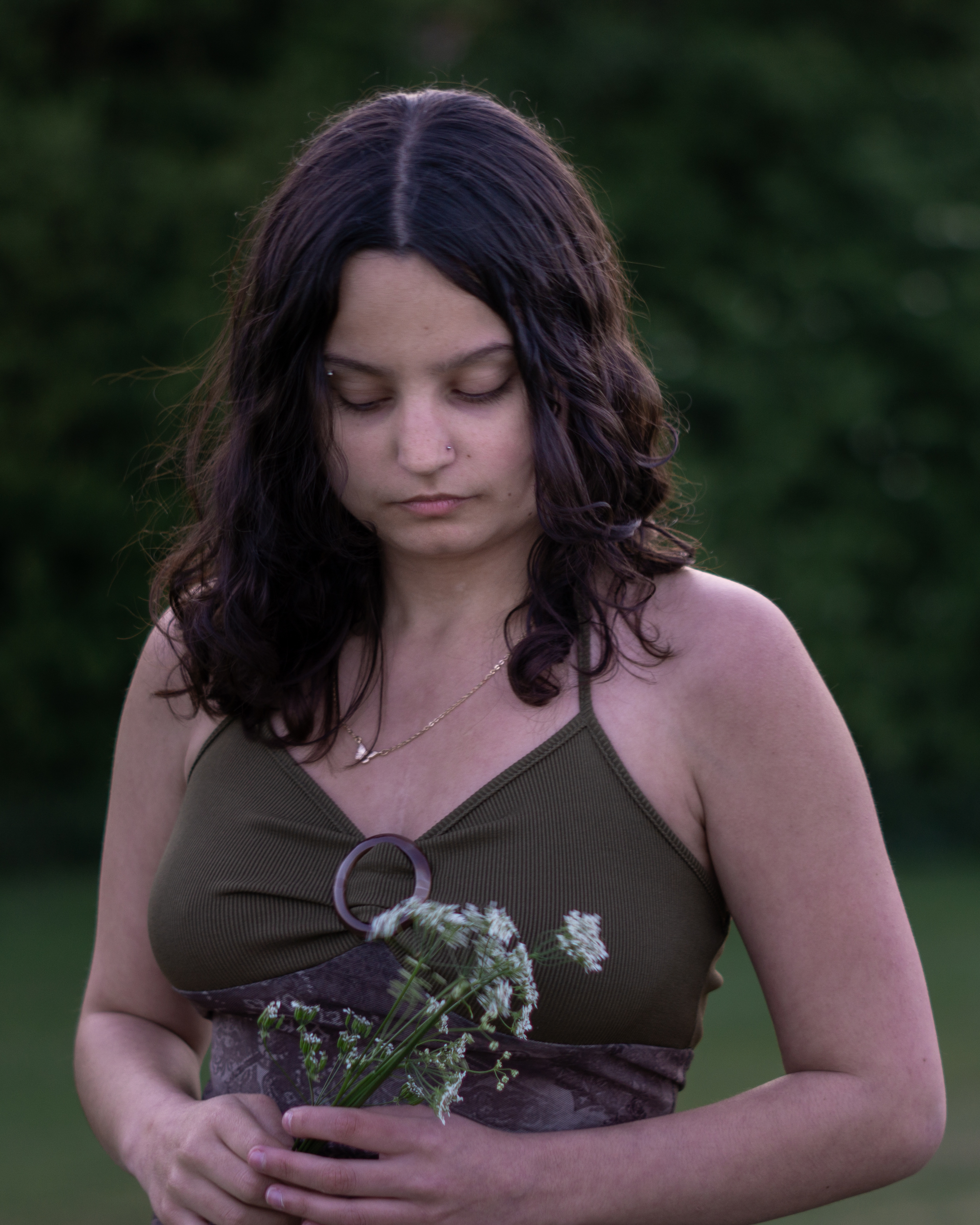 A woman dressed as a fae looking wistfully down at a bunch of flowers in her hands.