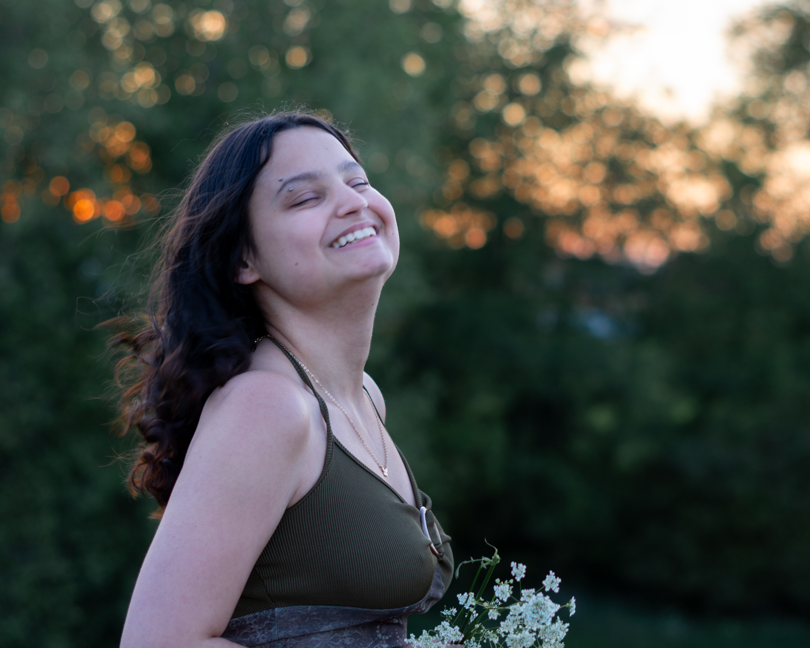 A woman dressed as a fae holding a bunch of flowers and smiling with her hair flowing in the wind.