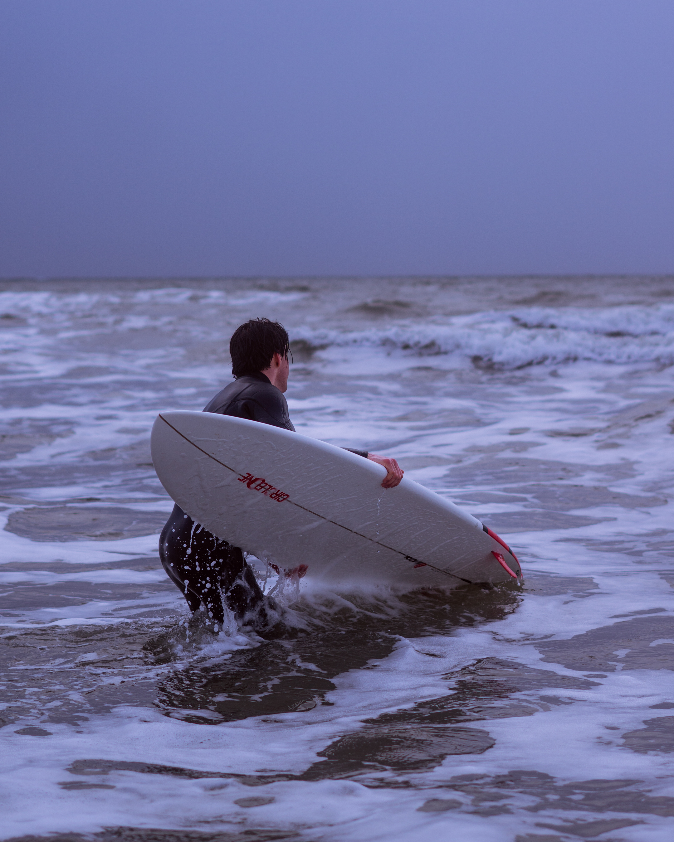 A man in a wetsuit clutching a surfboard while a wave approaches.