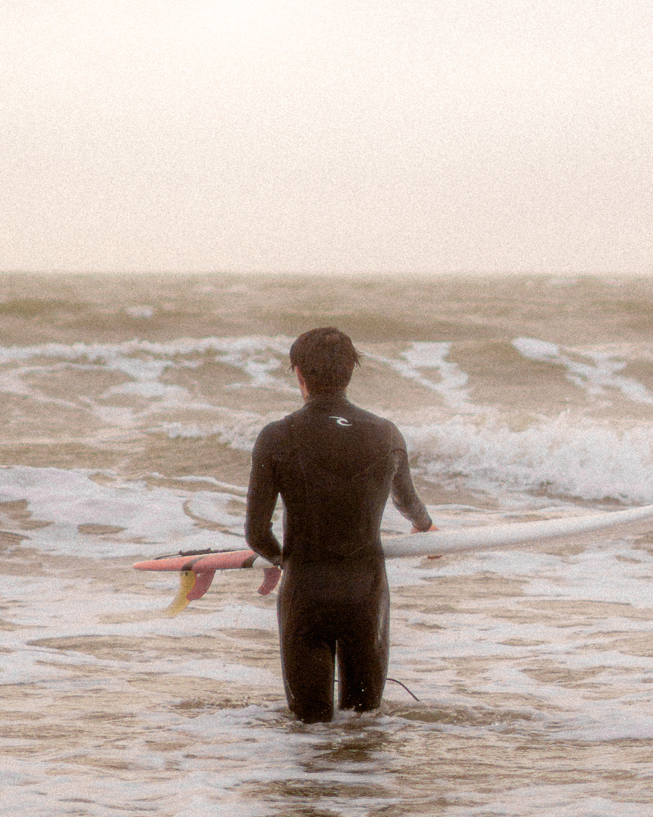 A man in a wetsuit clutching a surfboard while a wave approaches.